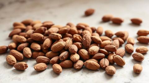 Whole unsalted almonds in their brown skins scattered on a pale stone kitchen surface
