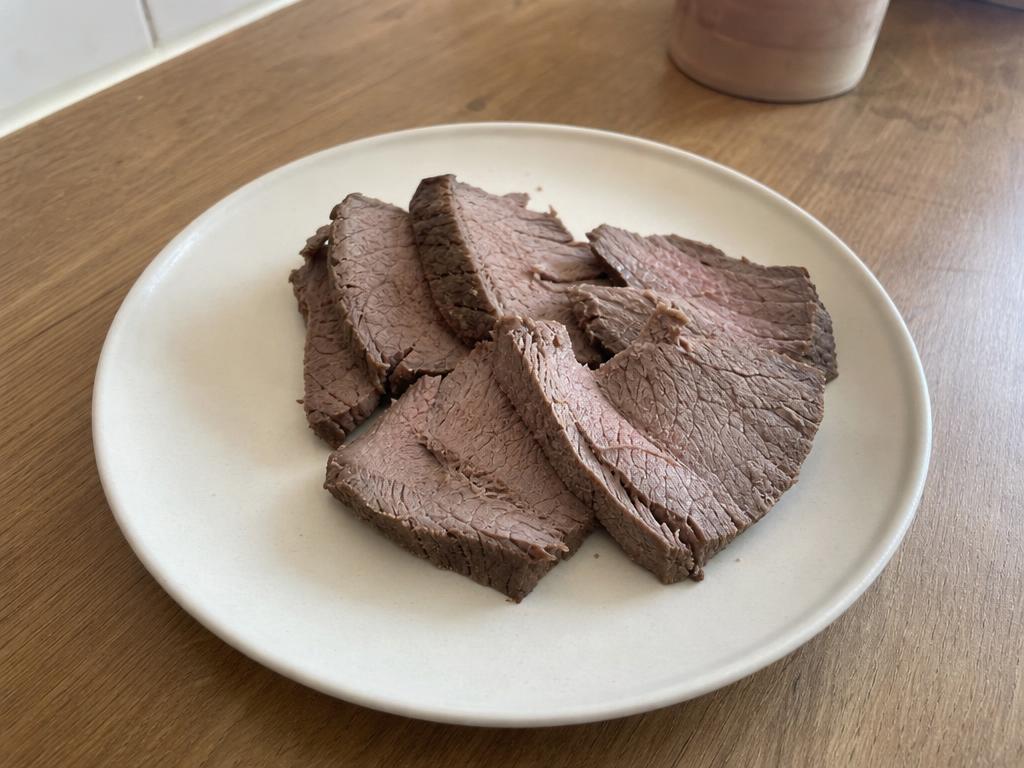 Slices of plain cooked lean beef on a light ceramic plate, with no seasoning or sauce