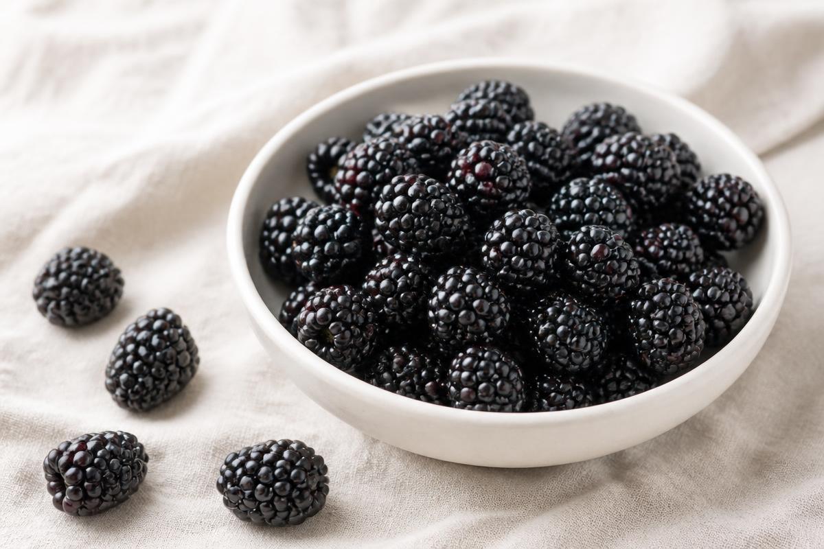 Fresh ripe blackberries in a small white bowl on a cream linen surface