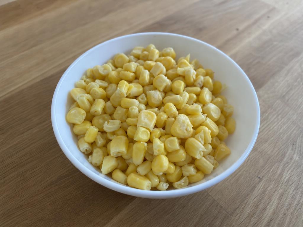 A white bowl of plain cooked yellow sweetcorn kernels cut off the cob on a light kitchen surface