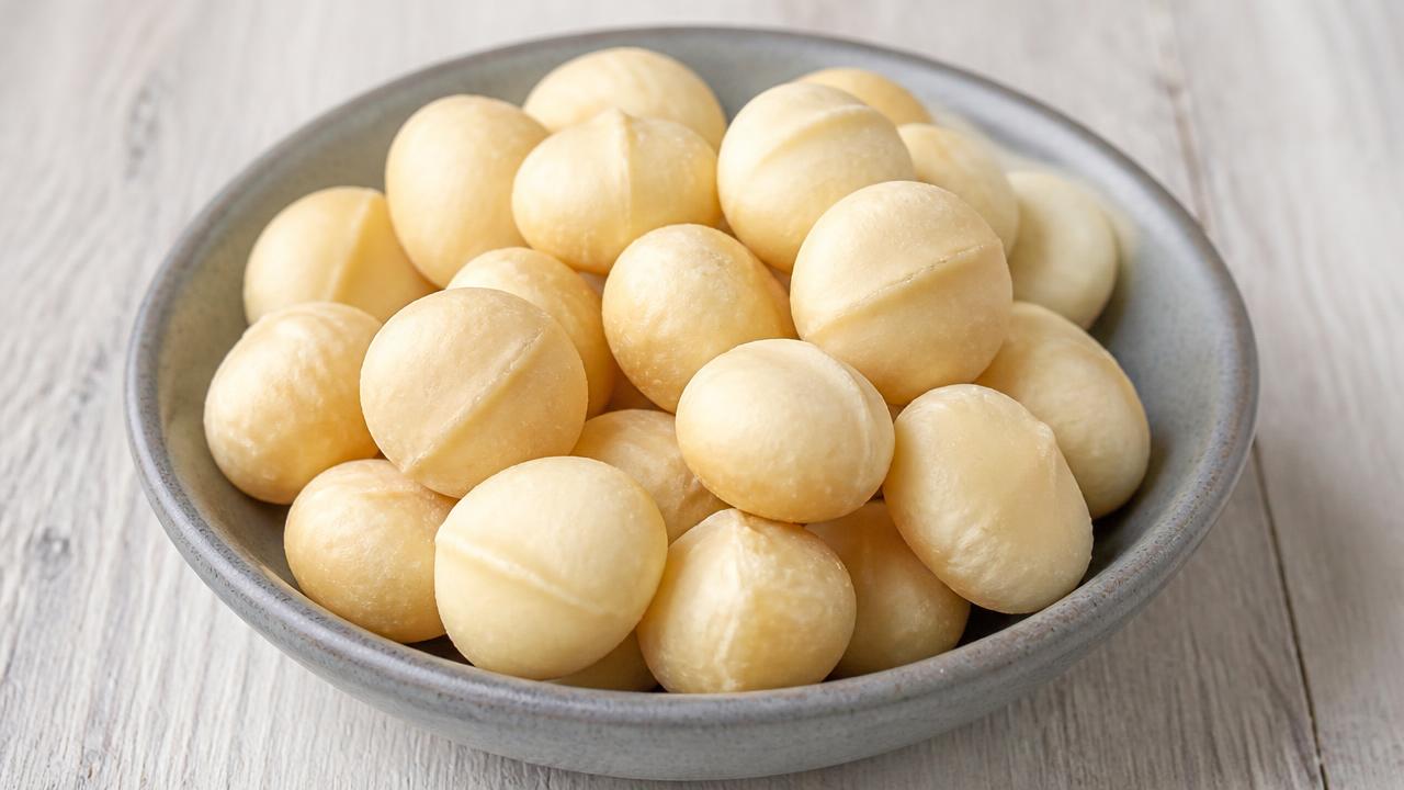 A grey ceramic bowl of plain shelled macadamia nuts on a pale wooden table