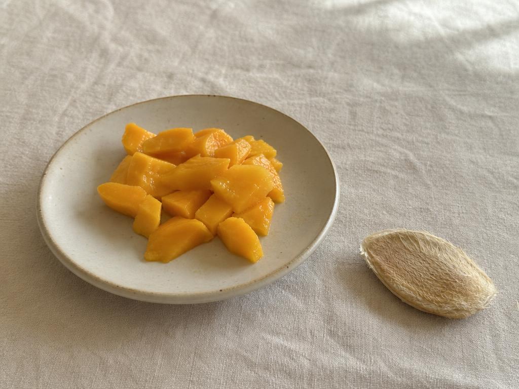 Ripe mango cut into small bite-sized pieces on a cream plate, with the large mango pit removed and set aside separately
