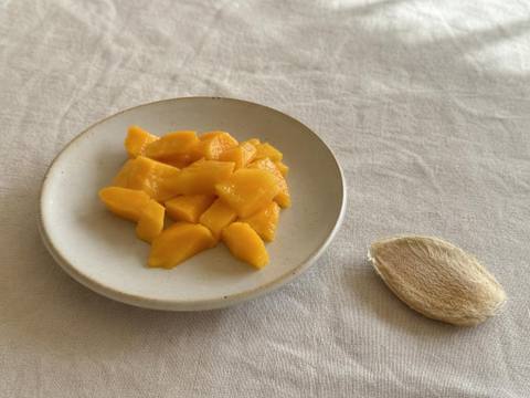 Ripe mango cut into small bite-sized pieces on a cream plate, with the large mango pit removed and set aside separately