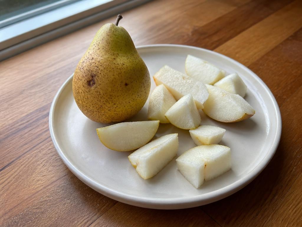 A whole speckled pear beside cut pear pieces with the core removed on a cream ceramic plate