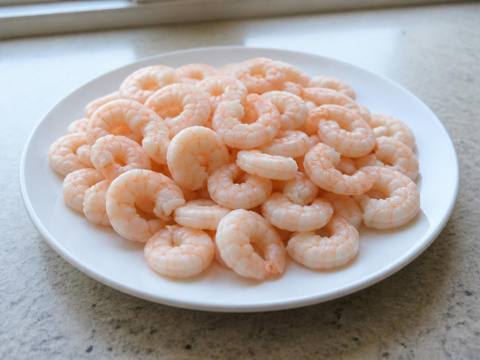 Plain fully cooked peeled shrimp with shells and tails removed, piled on a simple white plate with no sauce or seasoning