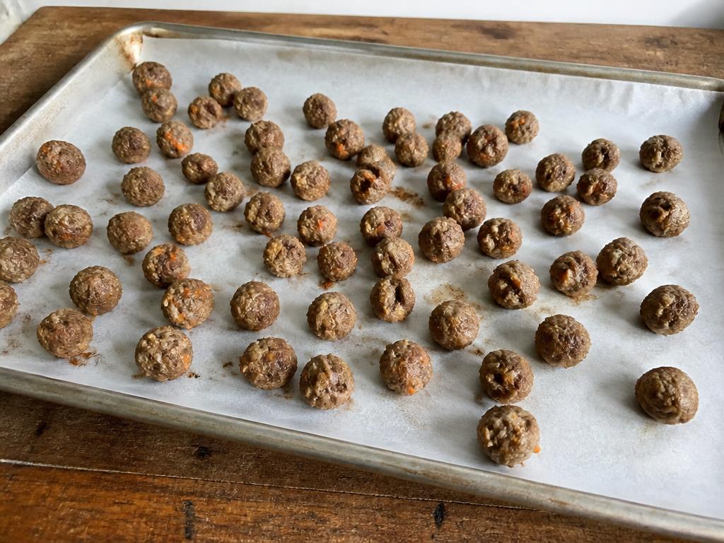 Small plainly cooked beef and carrot dog meatballs with visible carrot flecks on a baking tray