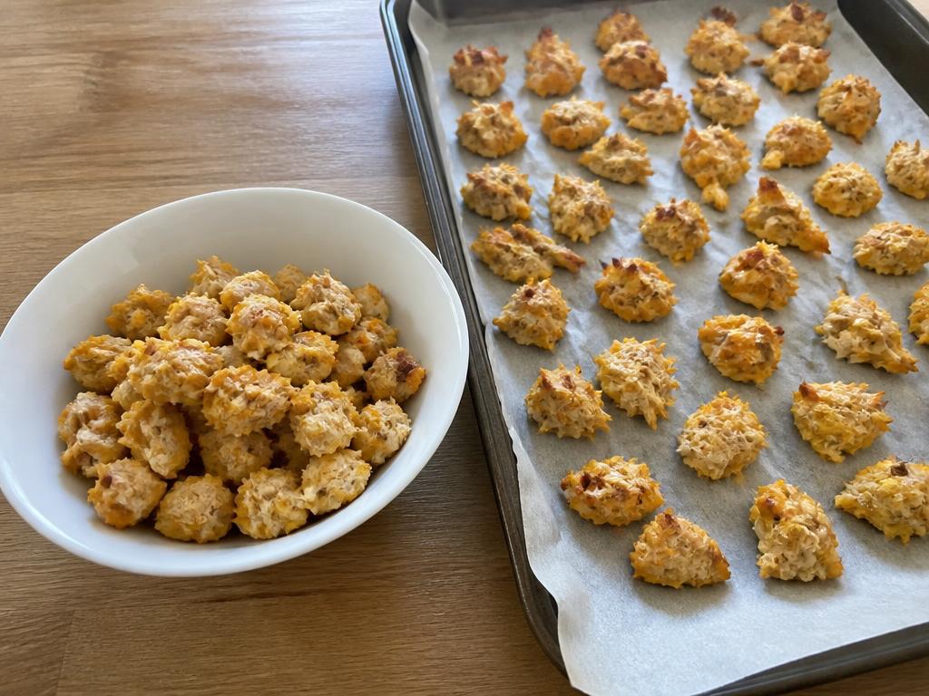 Small irregular baked training-size dog treats made from plain cooked chicken and sweet potato, in a white bowl beside a lined baking tray