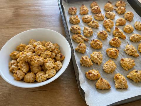 Small irregular baked training-size dog treats made from plain cooked chicken and sweet potato, in a white bowl beside a lined baking tray