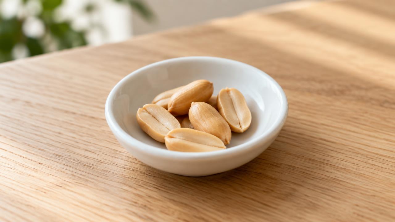 A few plain shelled peanuts in a small dish on a wooden table.