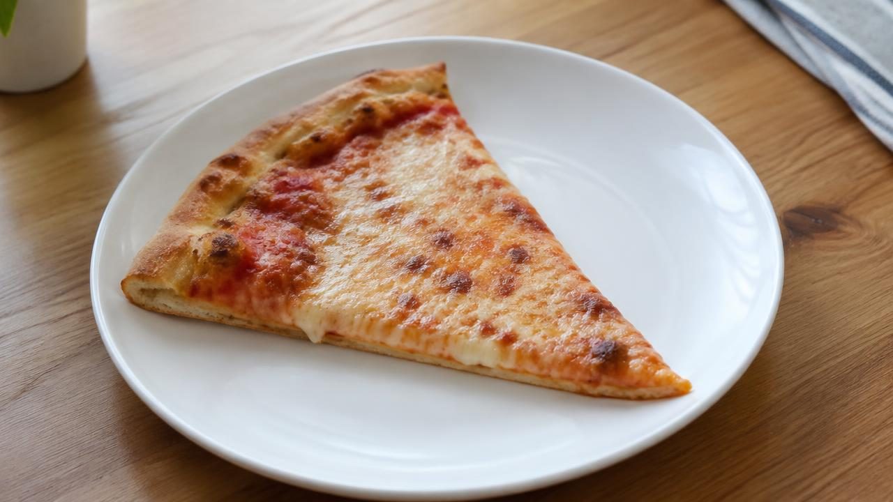 A slice of cheese pizza on a plate, shown as a food not to share with dogs.